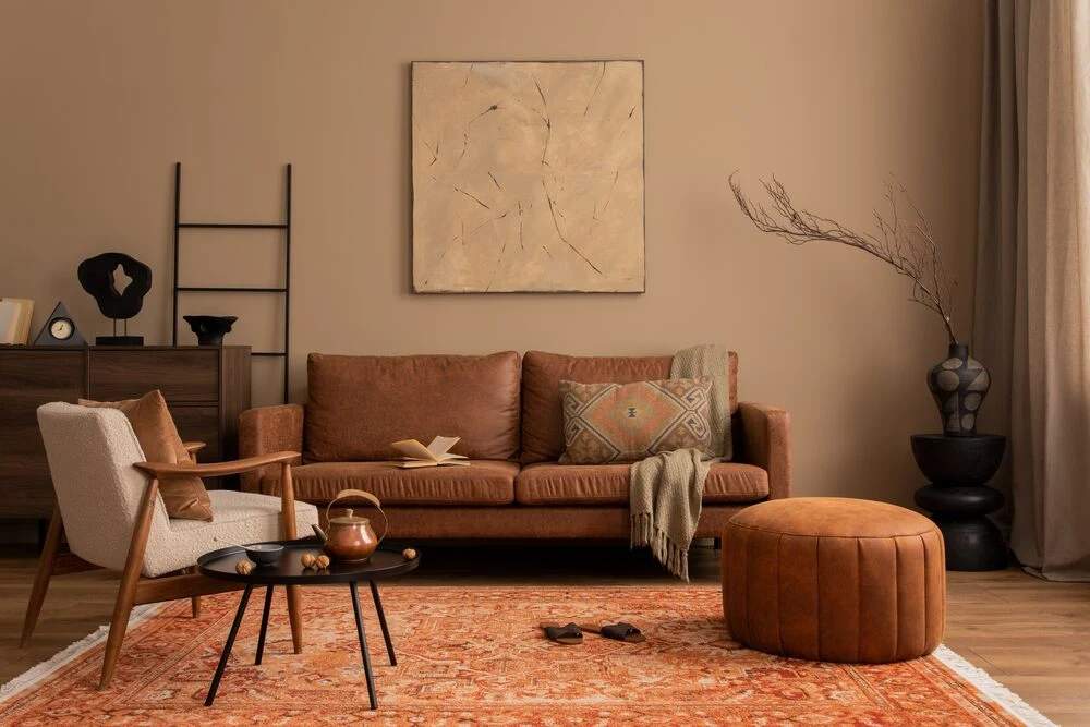 Stylish composition of living room interior with mock up poster frame, brown sofa, boucle armchair, round pouf, wooden sideboard, slippers and personal accessories.